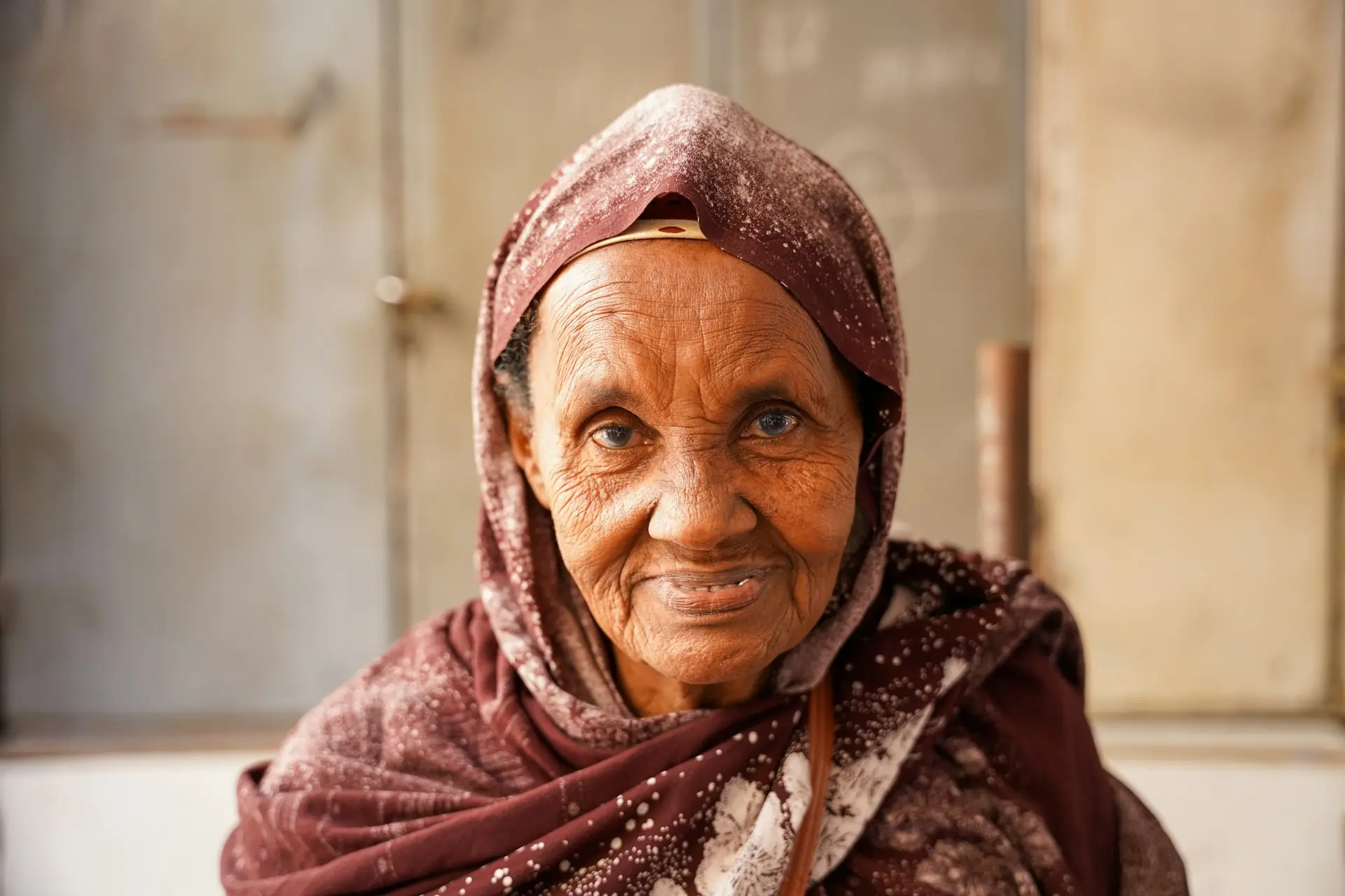 An older woman in a headscarf, smiling gently.