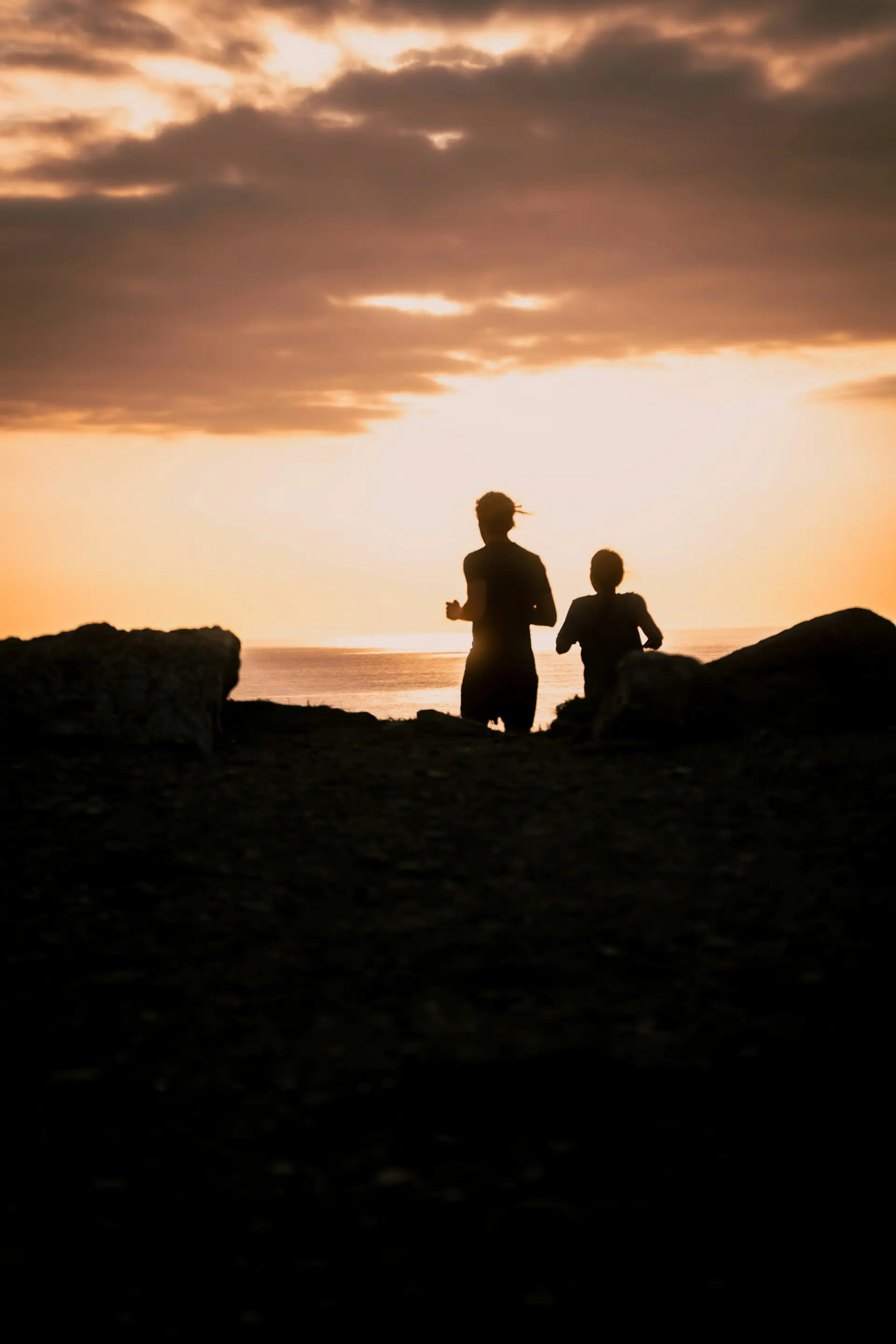 Two runners moving together, silhouetted against a golden sunset over water.