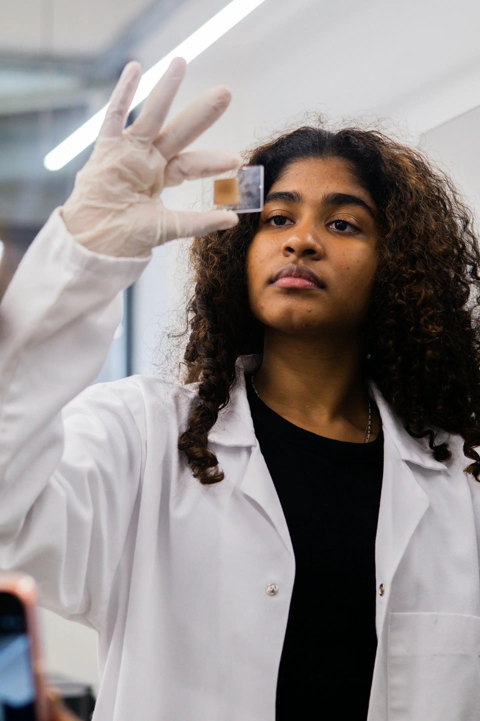Naledi in a white lab coat, examining a sample in the laboratory.