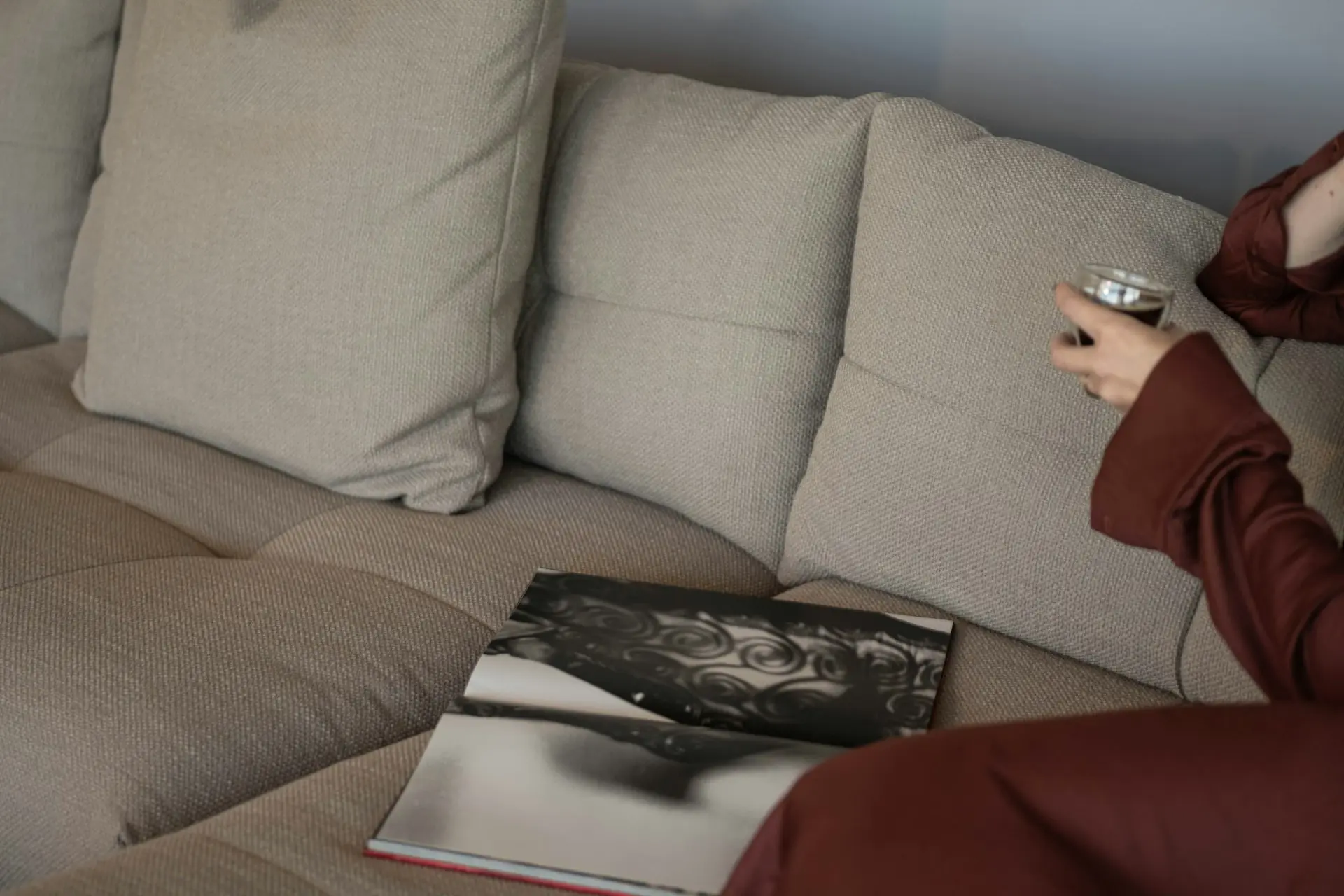 A woman resting on a sofa with a warm drink and a book.