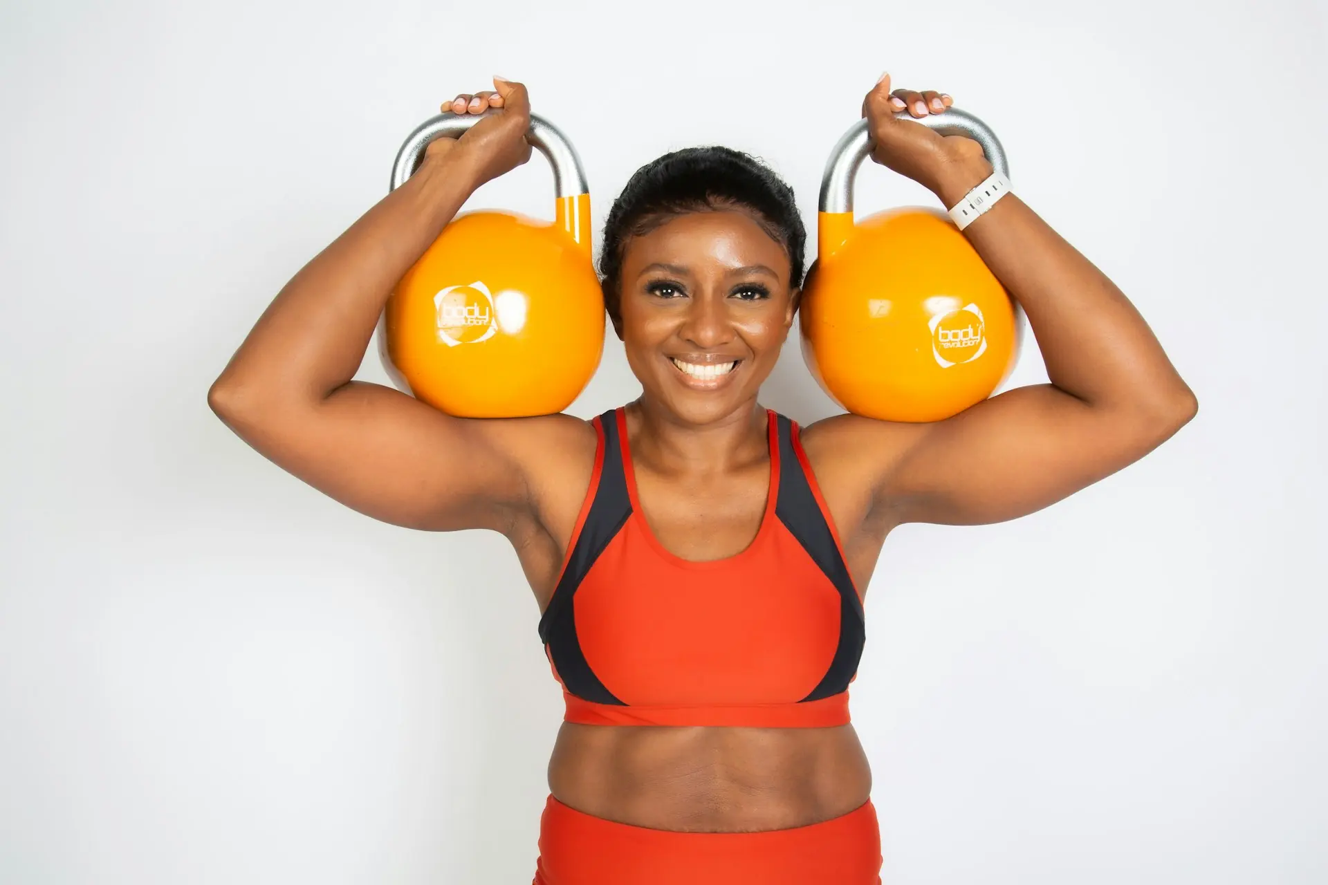 A woman pressing kettlebells overhead.