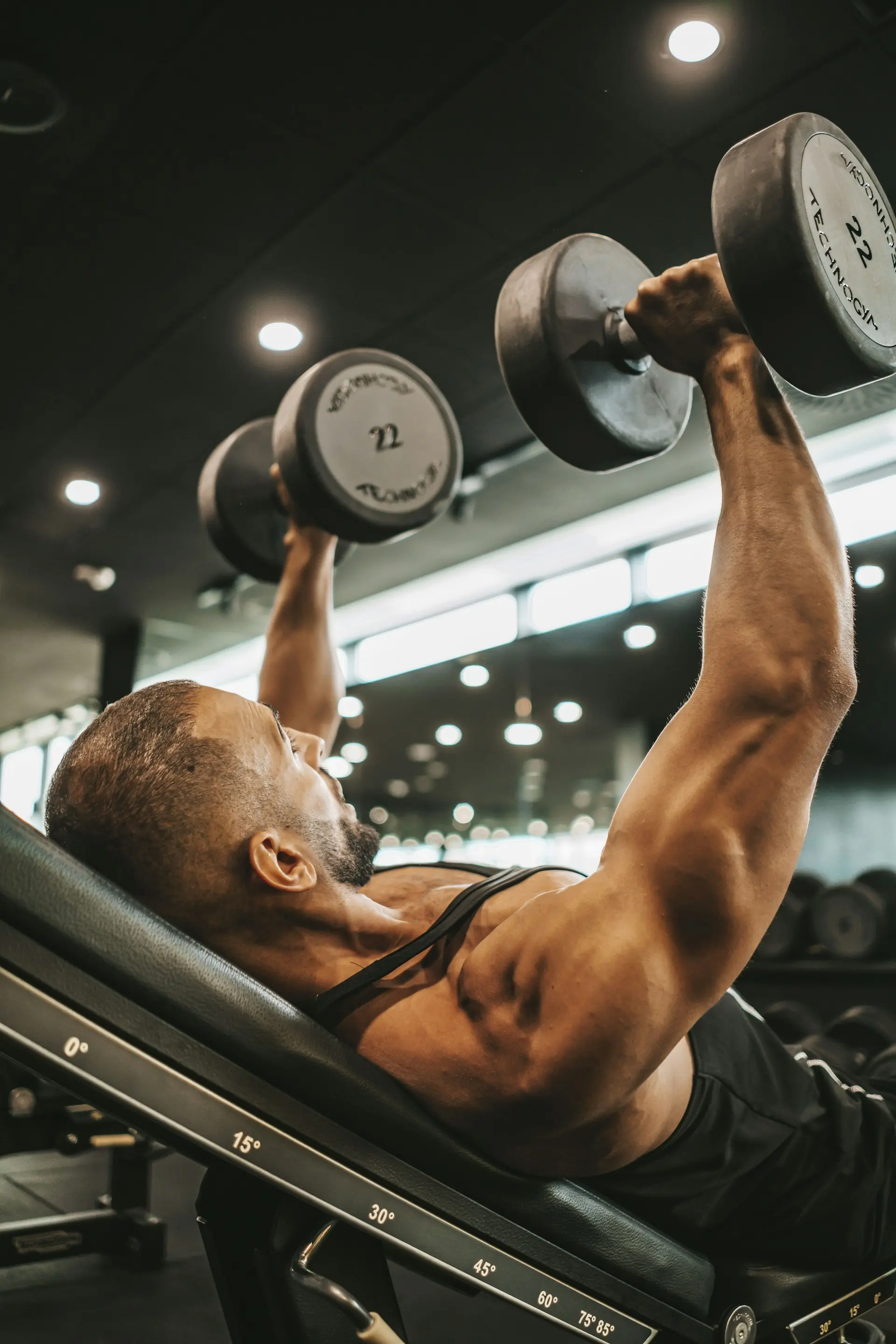 A man pressing dumbbells on an incline bench in a dark gym.