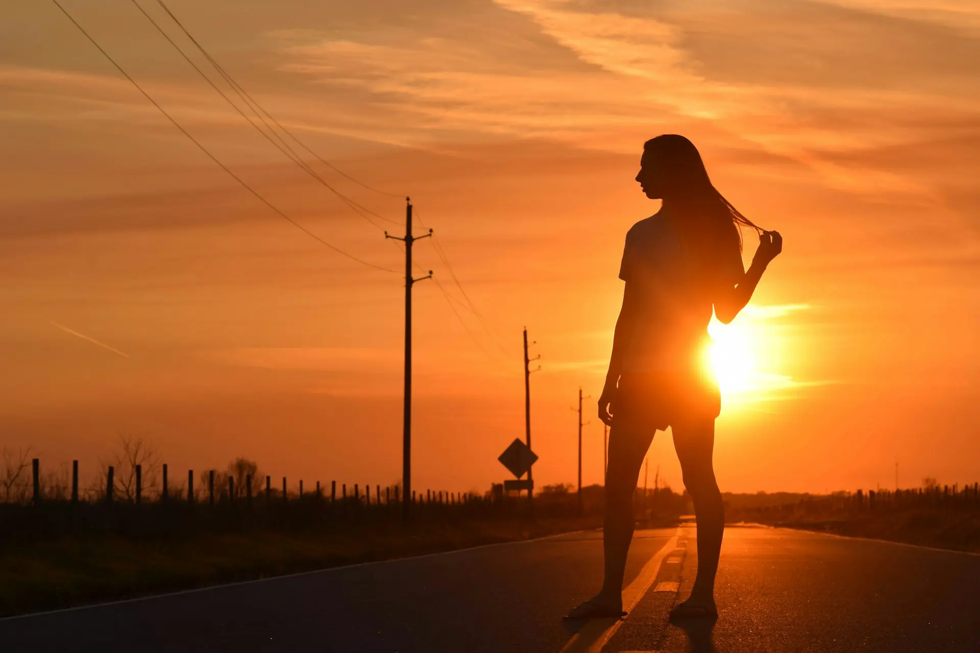 A woman silhouetted against golden-hour light on an open road.