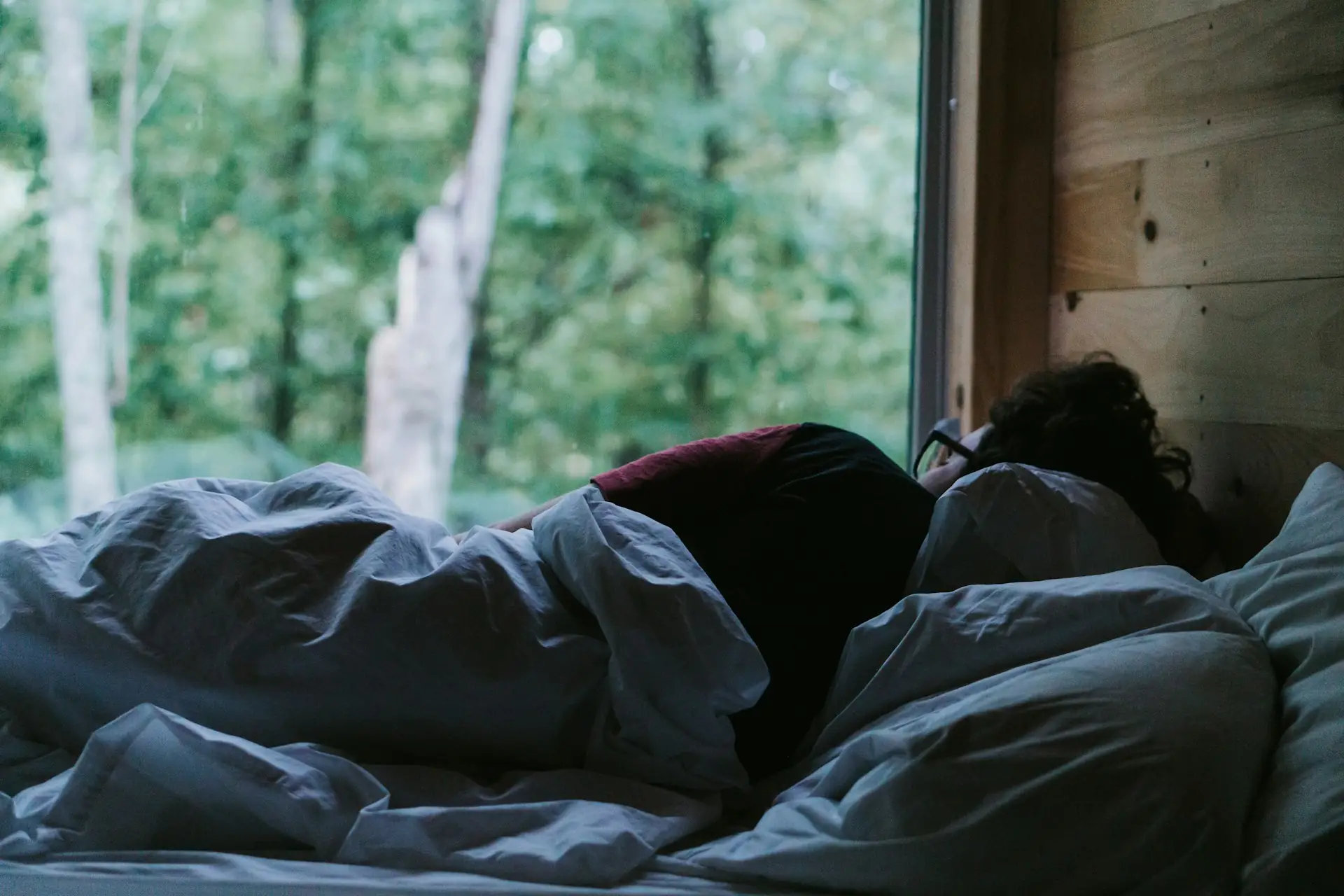 A person asleep under a blanket as light enters the room.
